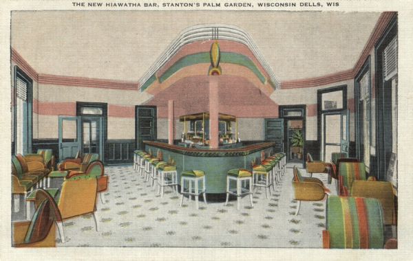 Postcard of the Hiawatha bar at Stanton's Palm Garden. There is a triangular bar at the center, and  tables and chairs lining the walls. There are multiple doors and windows surrounding the large room. The color was added to the image before it was printed. Caption reads: "The New Hiawatha Bar, Stanton's Palm Garden, Wisconsin Dells, Wis."