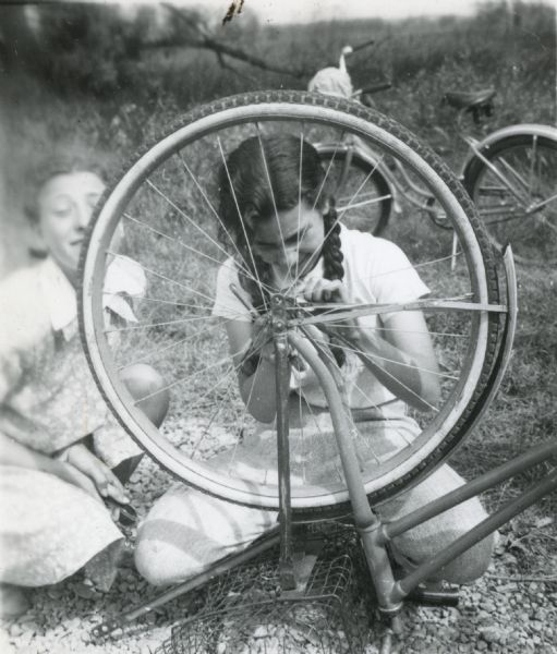 Girl (Theresa Castanga?) making adjustments to the front wheel of her bicycle on a bike hosteling trip in Madison sponsored by Neighborhood House.