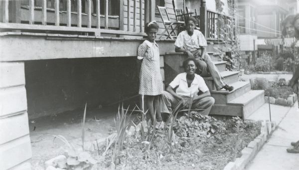 Image from the Garden Club record book kept by Neighborhood House, with Rosalie, Ollie Mae, and Adrena Matthews posing by their garden, near the front steps of their house at 617 Milton Street. Two other children (girls?), standing on the sidewalk, are barely visible in the frame.