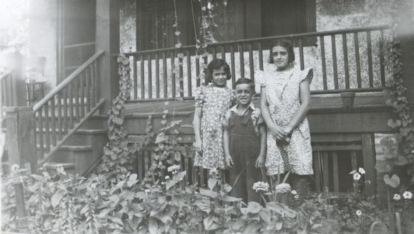 Image from the Garden Club record book kept by Neighborhood House, with Edith, John, and Caroline Cordio posing in the garden at the front of their house at 726 W. Washington Avenue.