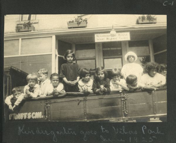 Children posing in the back of an open truck wagon in front of the Neighborhood House Infant Welfare Clinic. The wagon is marked "Frautschi". This is the first page of a snapshot album kept by Mary Lee Griggs, head of the  Parent Education and Play School programs at Neighborhood House.