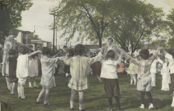 Hand-colored image from a scrapbook kept by Neighborhood House, with a group of children and two women playing a circle game outdoors.
