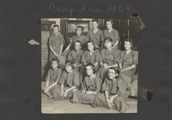 Page from an album kept by Neighborhood House, with a group of Camp Fire Girls posing on and around a sofa. The Camp Fire Girls was one of many youth groups sponsored by the settlement house.