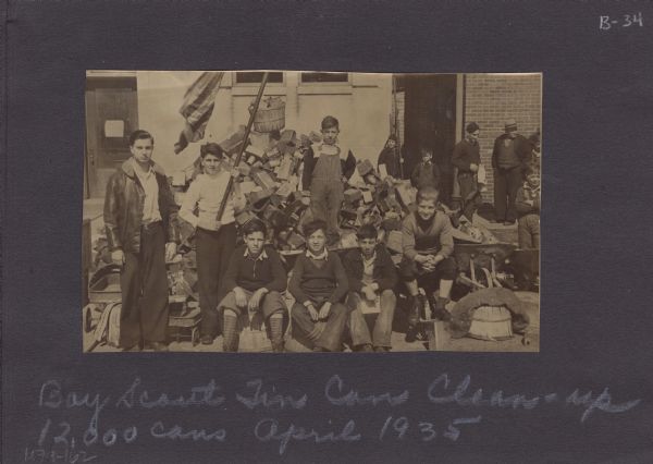 Page from an album kept by Neighborhood House, with a group of Boy Scouts and some of the 12,000 tin cans they collected in a neighborhood clean-up campaign.
