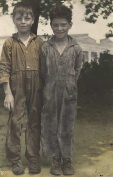 Hand-colored full-length portrait of Sam Cimino and Sam Romano, "2 neighbors and members," who are standing in the shade of a tree and dressed in overalls, from a scrapbook kept by Neighborhood House.