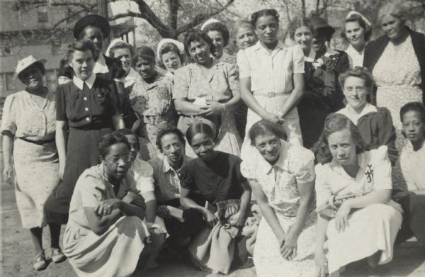 Image of outdoor group portrait from a scrapbook kept by Neighborhood House, with members of a Red Cross home nursing class held January-May 1942 at the settlement house. Women were trained to assist the wounded in case of attacks directed at civilian populations.