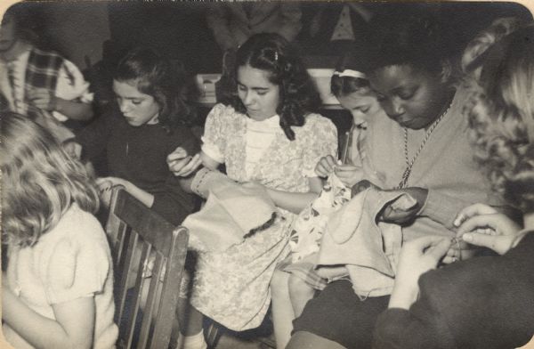 Image from a scrapbook kept by Neighborhood House, with girls sewing in a handicraft group.