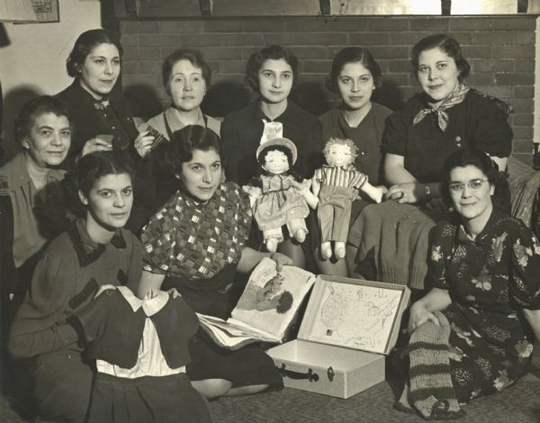 Members of the N.B.B.O. Club at Neighborhood House, posing with the contents of a suitcase they put together to send to a five-year-old girl in Spain. The club was established in 1931 as a social club for young women at the settlement house. Part of a project to promote "World Friendships Among Children," the club members spent two months making clothing, a scrapbook, and dolls to fill the suitcase. Head resident Gay Braxton is at the far left, and Mary Lee Griggs is third from the left in the back row.