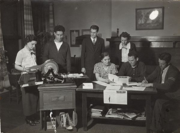 Members of the Nu Pi Chi (Neighborhood Press Club) working on the first edition of "The Neighbor," a newsletter printed at Neighborhood House. Pictured from left to right are Tina Nania and Sam Namio operating the press; seated are Nellie Navarra, women's editor; Joe Germano, men's editor; Steve Caravello, sports editor; and standing in the back, S.L. Chaney and Dorothy Wolfe, advisors.