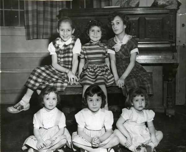 Group of six girls, three sitting on a bench L to R: Dolly O'Meara, Rozanne Petratta, and Mary Louise Masino, with a piano behind them, and the other three sitting cross-legged on the floor L to R: Nikki Masino, Regina Ann Masino, and Toni Capadona.