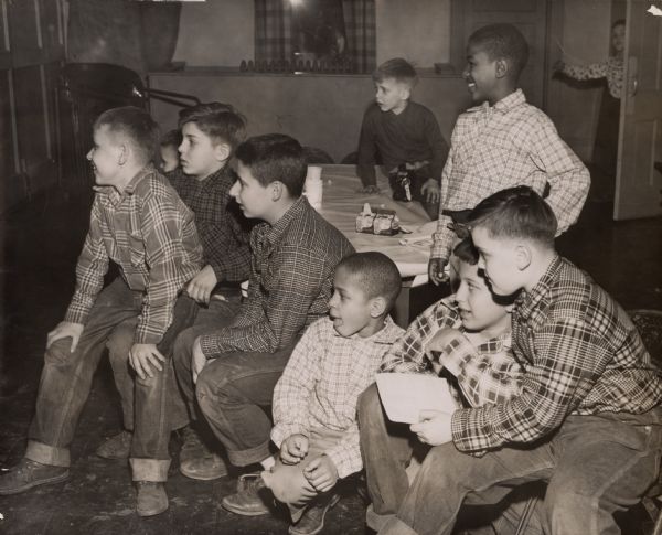 "While others played games, this group of boys 'coached' from the sidelines." (photo caption in <i>Wisconsin State Journal</i>), L to R: Edward Abbott, John DiSalvo, Henry Cuccia, Larry Stodesville, Charles Cerniglia and Thomas McCarthy. Standing behind McCarthy is Alfonso Stodesville. The boy behind Alfonso is unidentified. They are sitting, standing, or kneeling by a covered table set for snacks or crafts. 