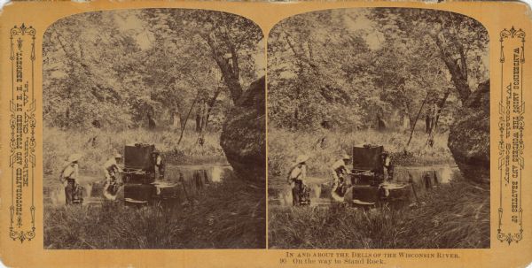 Stereograph of Bennett's crew hauling a portable darkroom through a pond of water. They are on their way to Stand Rock. Text at right: "Wanderings Among the Wonders and Beauties of Wisconsin Scenery."