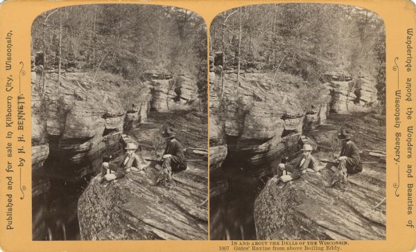 Elevated view of two men sitting on the side of a rock formation. The man on the right is holding a rifle and a stringer of squirrels. The man on the left is holding an axe. Below them on the shoreline is a boat. Text at right: "Wanderings Among the Wonders and Beauties of Wisconsin Scenery."