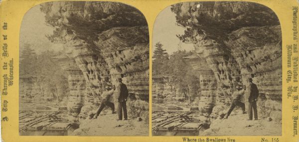 Two people standing on a rock formation looking towards the river. One man appears to be skipping stones. There are large rafts along the shoreline. Text at left: "A Trip Through the Dells of the Wisconsin."