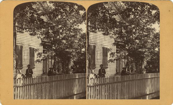 Two women and a girl in the fenced yard at the Bennett House. One of the woman may be Harriet Bennett. The girl is holding a dog.