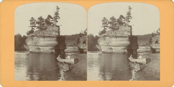 Three girls at Sugar Bowl. Two girls sit in a rowboat while the third sits on the shore, dragging a stick through the water. In the background a man is standing on a beach.