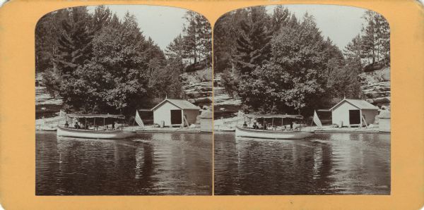 View from water of a tour boat with an American flag near a boathouse on the shoreline of Mirror Lake.
