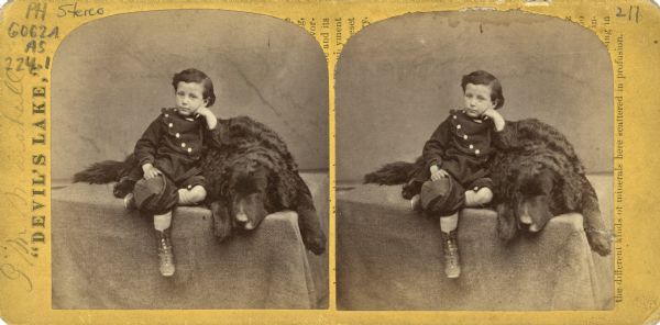Stereograph of Ashley Bennett, the son of photographer H.H. Bennett, posing beside a dog. The print is pasted on the reverse side of the print, over text.