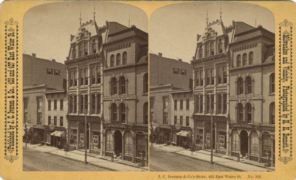 Elevated stereograph of J.C. Iversen and Company on the west side of Water Street (north of Grand Avenue). Other stores include: Adam Koch Restaurant and Quin's Antiquarian Book Store/Manufactory. Men are standing on the sidewalk, and there is a cigar store or wooden Indian in front of a storefront advertising cigars and tobacco. Text at right: "Milwaukee and Vicinity, Photographed by H.H. Bennett."