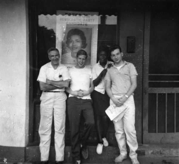 In the summer of 1964, Freedom Summer volunteers pose in front of a campaign poster for Victoria Jackson Gray, Mississippi Freedom Democratic Party candidate for Congress representing the 5th District.  Photo is likely taken outside of the Victoria Jackson Gray's MFDP headquarters.
