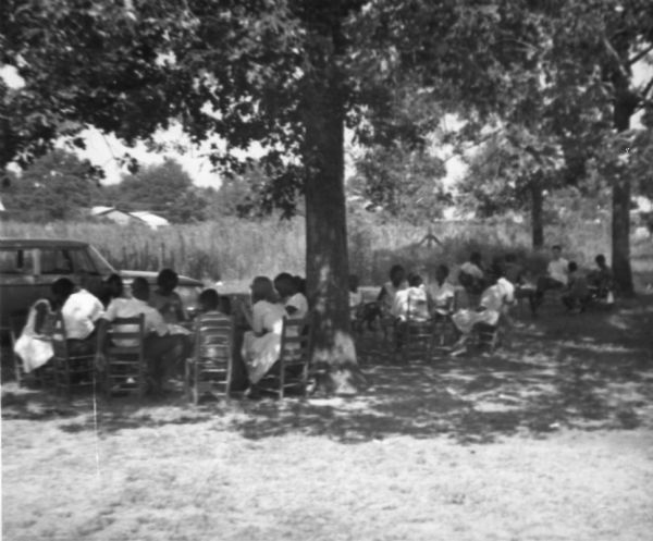 Groups of students attend class during Freedom Summer as they sit outside in the shade.  Likely at the Freedom School, Priest Creek Baptist Church.
