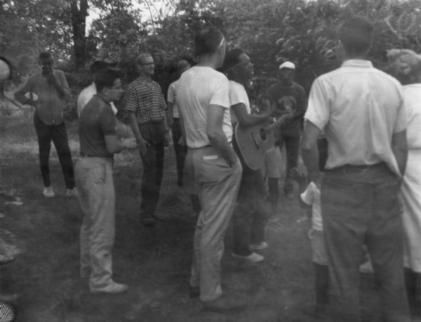 A group of adults and children at an impromptu concert held outdoors during Freedom Summer outside of the Freedom School at Priest Creek Baptist Church. Likely participating in music workshops that were a part of the Mississippi Summer Caravan of Music.