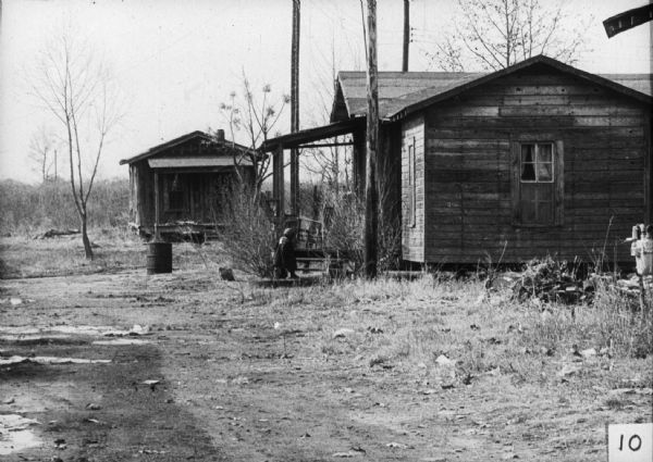 Two homes along a dirt road with a small child on the front porch of the nearest house.