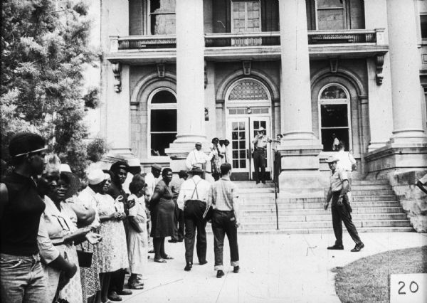 A line of predominantly African-American people likely outside of the Leflore County Courthouse, probably at a voter registration drive. Caucasian law enforcement officers look on.
