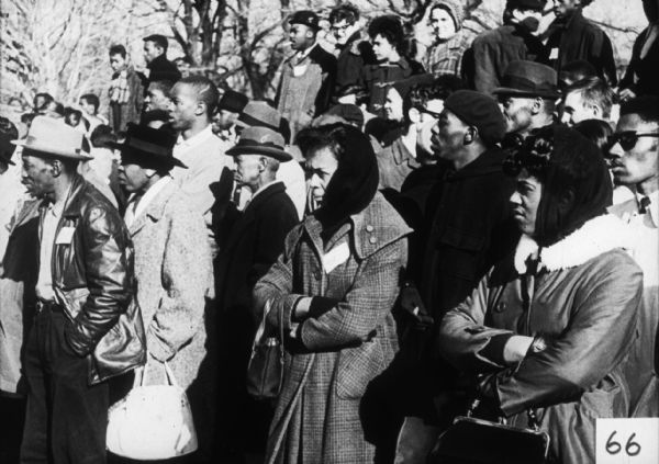 An integrated group of people stand outdoors in coats and hats.