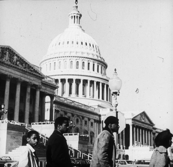 Four people walking past  the U.S. Capitol building likely protesting Congress' opening day.