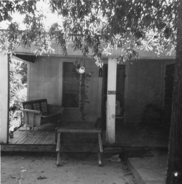 Exterior of a home taken by a civil rights volunteer.  "The front porch of our home at Mrs. Willie Thompson's, 808 Augusta, McComb, Mississippi. The house was on a street that had no lights and was unpaved. We could not remain on the porch during heavy rain, but it was a welcoming cool spot in the early morning and late evening. [...] Reverend Clare Nesmith and I were sitting here when two white men came, greeted us quite warmly, and went inside to see Mrs. Thompson. The Thompson's daughters were about finished with cleaning the car. The two white men came out and the driver purposefully gunned the motor, sending great dust from the always unpaved road onto the cleaned car. The girls had to start over their cleaning job."