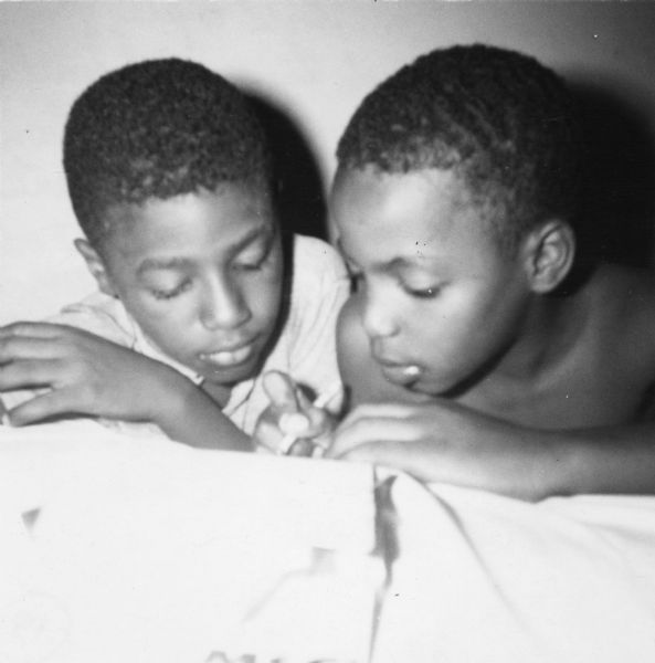 Two boys in an image taken by a civil rights volunteer.  The boy on the right, identified as Charles, is writing while the boy on the left, James, looks on.  "Charles and James loved to play games with me even though they waited sometimes until after 9:00 p.m. for me to return home.  Charles (right) especially wanted to be with me as often as possible.  Charles also walked with me to the Freedom School.  He wanted to canvass with me in Summit, but I felt it was an unnecessary risk for him."