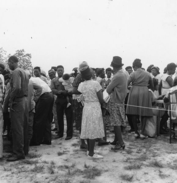 A line of African-American men and women wait in a line that approaches tables outdoors at a primary election for the LCFO (Lowndes County Freedom Organization).