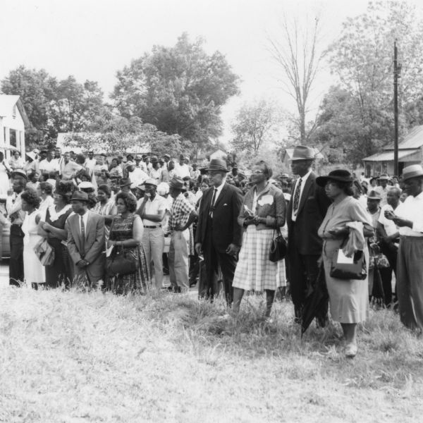 A large group of people gathered outdoors on a lawn at a primary election for the LCFO (Lowndes County Freedom Organization). There are buildings in the background.
