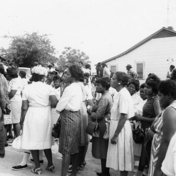 A large group of people standing outdoors at a primary election for the LCFO (Lowndes County Freedom Organization). There is a building in the background.