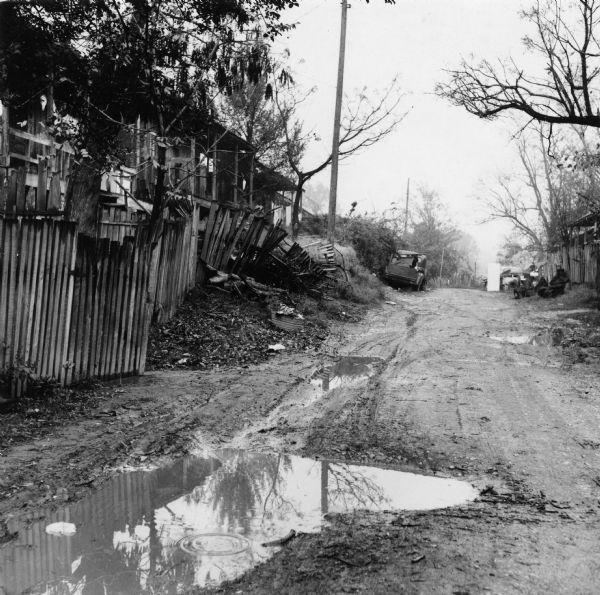 A wet and muddy dirt road in the Beekman Quarters neighborhood in Natchez, Mississippi. "No pavements, no drainage system, no streetlights, no sewers. No nothing."<p>Beekman Quarters housed 81 people in 23 buildings. None of the houses in the neighborhood had running water or gas/electric heating; the neighborhood had 15 outdoor toilets and 11 outdoor water hydrants.