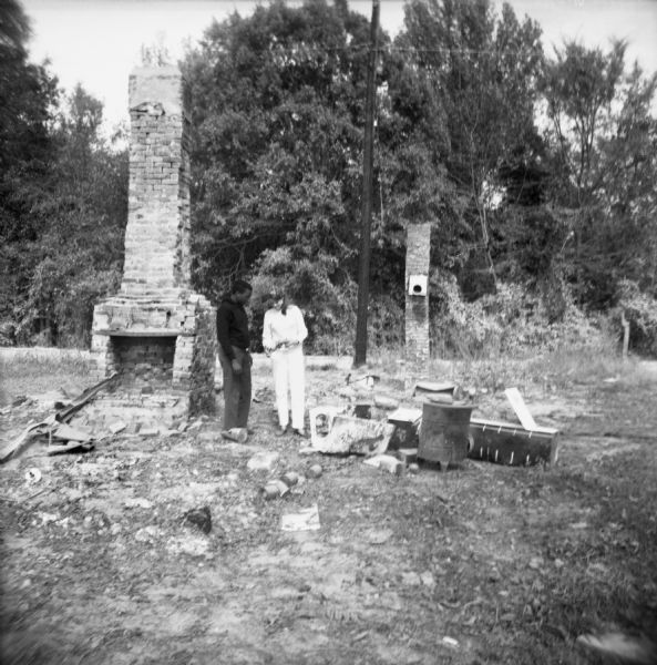 A man and a woman stand near a fireplace and other rubble of a burned Freedom House used by civil rights workers. The house was "burned down in the middle of the day in early September."