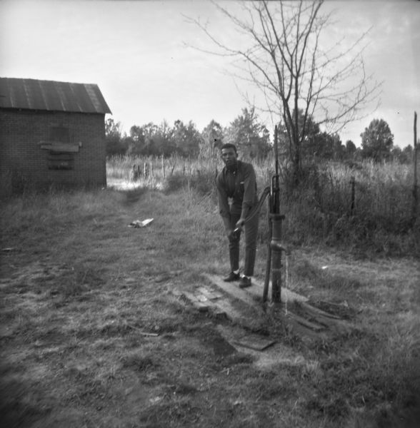 A man hand pumps water in the yard outside of White Station Freedom House. "In all the rural Freedom Houses (and <u>all</u> rural houses) wells and outhouses are the order of the day. This is White Station's pump."
