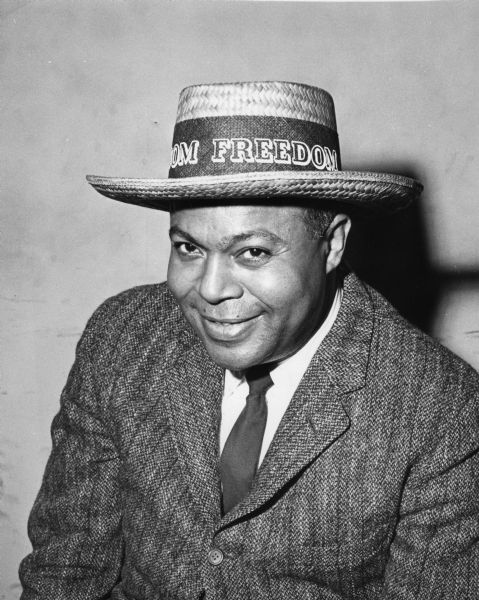 Portrait of James Farmer, civil rights activist and co-founder of CORE (Congress of Racial Equality). He is wearing a straw hat with a band that reads "[...]OM FREEDOM."