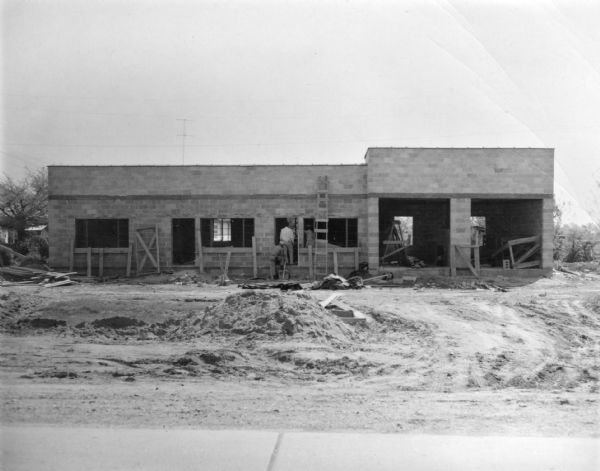 A Pan-Am Cafe and Service Station while under construction. Three people are standing near the doorway. The station was owned by Amzie Moore, noted civil rights activist.