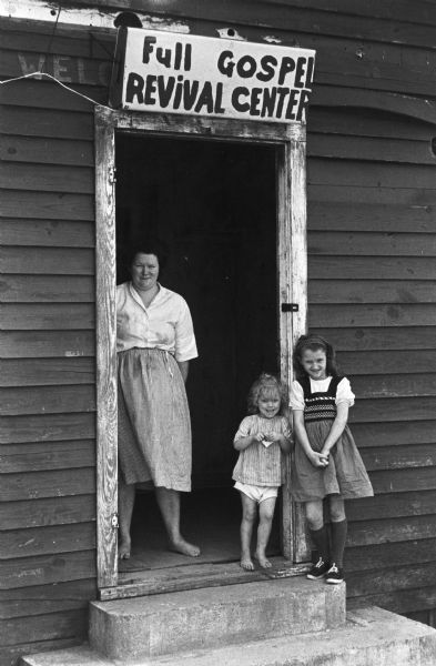 A woman and two girls stand at the open doorway of a building. A sign above the door reads "Full Gospel Revival Center." The image was taken by a civil rights volunteer.