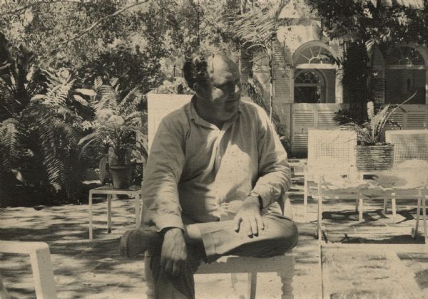 De Antonio seated in an outdoor courtyard at the Tree's Barbados estate. He is looking to his left and has one leg crossed over his knee.