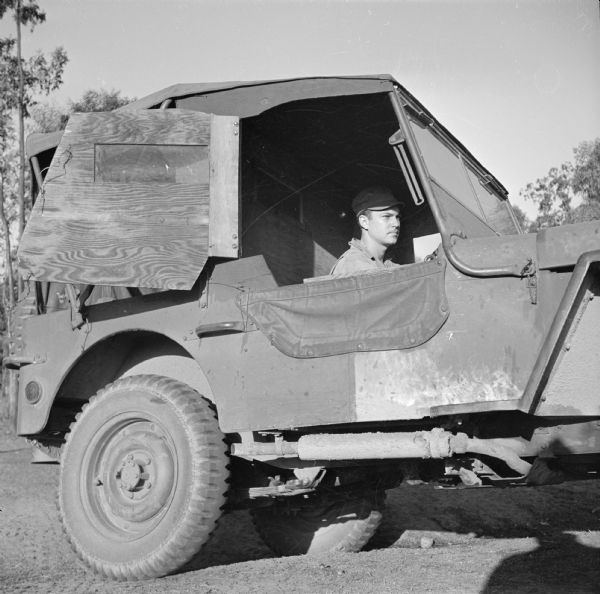 Corporal Earl Foster, a mechanic in a quartermaster unit, of Kenosha, Wisconsin, at the wheel of a jeep sedan at Camp Cable, near Brisbane, Australia. Driving an open jeep in the winter can be a chilly job, so the soldiers built a plywood cab.