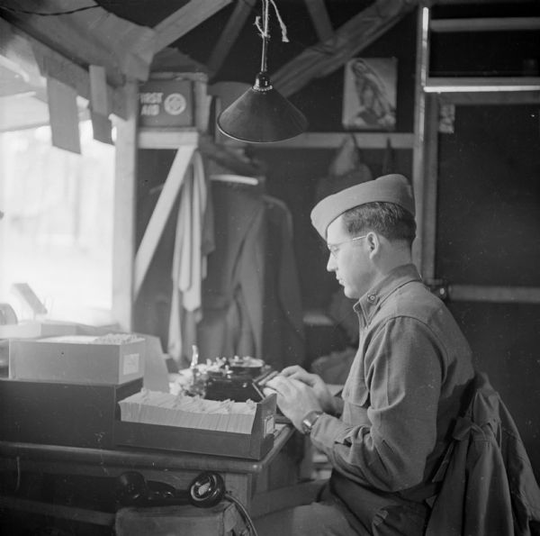 Red Cross Field Director, G. Robert Mowerson of Ann Arbor, Michigan, works at his typewriter at Camp Cable, near Brisbane, Australia. A field telephone is in the foreground.