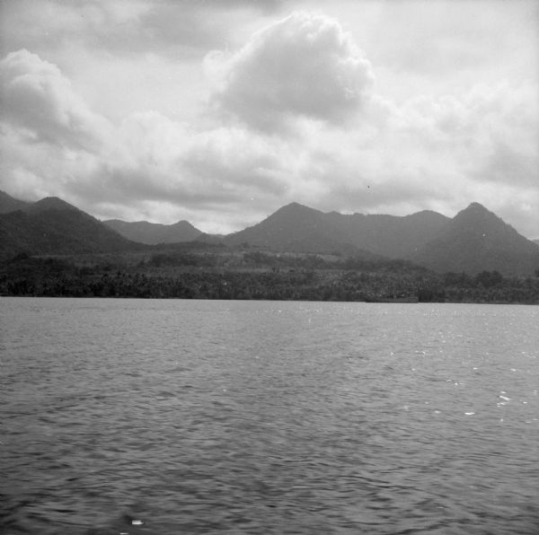 A view of Milne Bay, New Guinea (present day Papua New Guinea), from the sea. A ship can be seen on the right, at the shoreline.