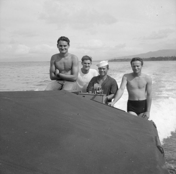 Crew of four aboard a Higgins boat, also known as a LCVP, which stands for "Landing Craft, Vehicle, Personnel." Their names, left to right, are Fireman 1st Class Alex Georgeson (shirtless) of Portland, Oregon, Private George Goldstein of Youngstown, Ohio, Boatswains Mate 2nd Class Walter Barton of Los Angeles, California and Seaman 1st Class William Black (shirtless) of Durango, Colorado. The photograph was taken on Milne Bay, New Guinea (present day Papua New Guinea).