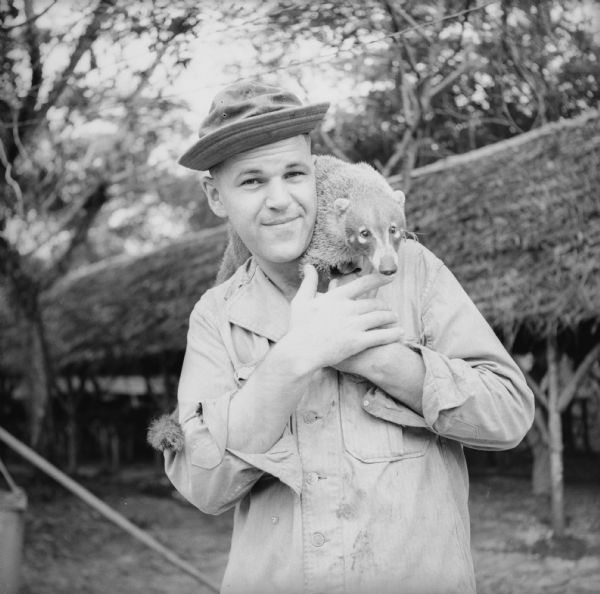 Corporal Marcell Vanden Heuval, from Grand Rapids, Michigan, poses with his coati named "Speedy" perched on his shoulder. He was a cook at the military camp on Kiriwina Island in the Solomon Sea, New Guinea (present day Papua New Guinea). Coatis are South American mammals related to raccoons.