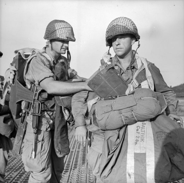 Paratroopers at a Drome (airfield) near Port Moresby, preparing to take off for a landing at Nadzab near Lae. Lae is a Japanese-held airfield in New Guinea (present day Papua New Guinea). One soldier is checking the gear of another.