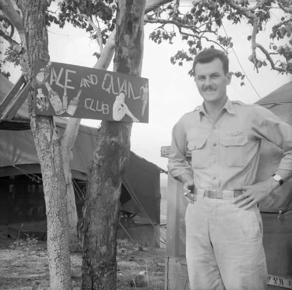Lieutenant Colonel Harry J. Bullis of Portland, Michigan, poses next to the sign for the "Ale and Quail Club" on a military base in Port Moresby, Australia. Robert Doyle's notes indicate he is in a Bomb Group.
