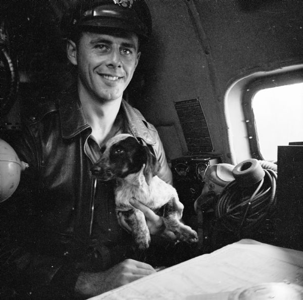 Lieutenant Paul Seramur of Milwaukee, Wisconsin, at the navigator table in a Consolidated B-24 Liberator warplane during the Alexishafen strike. He is holding his pup, "Cobber." Alexishafen was a Japanese occupied airbase located on the northeast coast of New Guinea (present day Papua New Guinea), near Madang.
